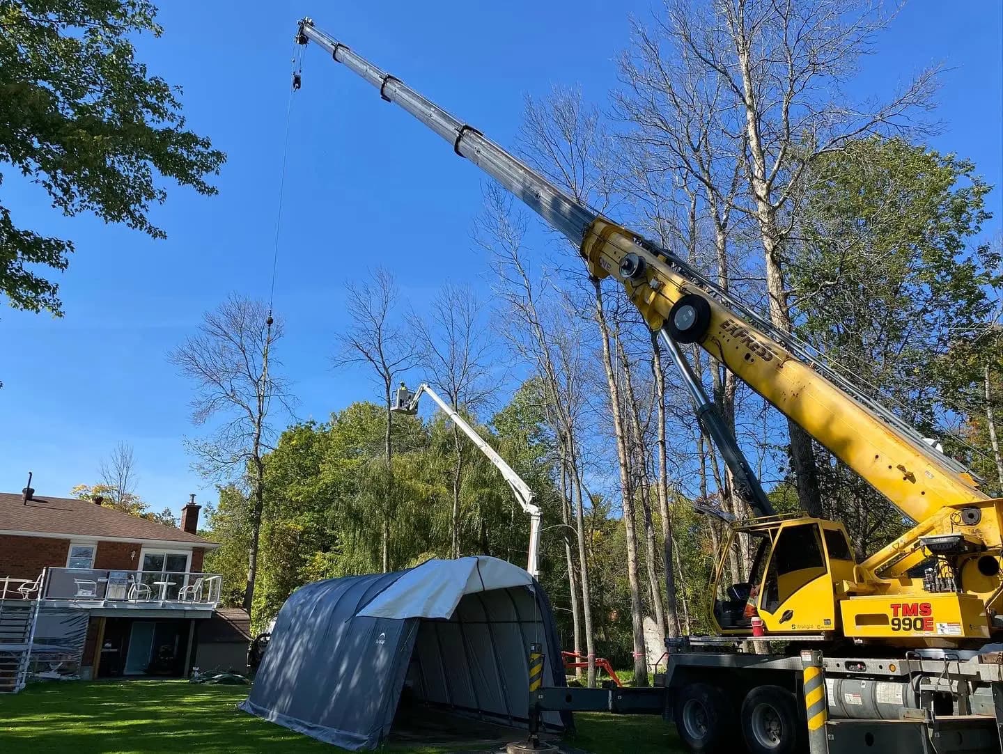 Tree removal crew using crane and chainsaw to safely remove a large tree from a residential property in Simcoe County